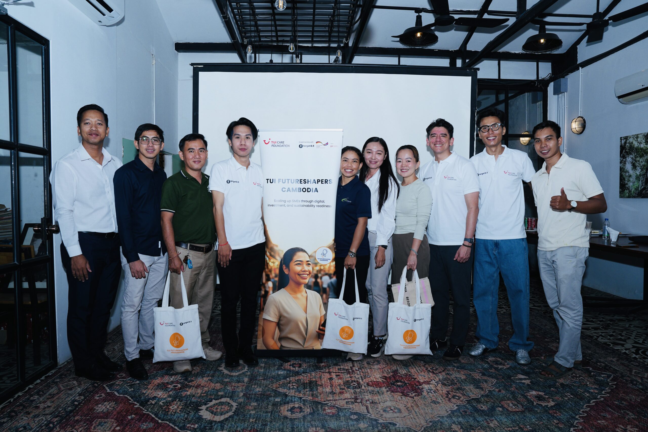 A group of people posing next to the TUI Futureshapers Cambodia sign and smiling